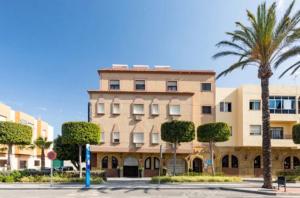 un grand bâtiment avec un palmier en face dans l'établissement Hostal La Costa, à El Ejido