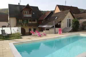 a swimming pool with two pink chairs and a house at les Gîtes 2-4 pers Rémy HEROLD in Katzenthal