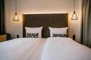 2 camas en una habitación de hotel con sábanas y almohadas blancas en LOOM Hotel & Skybar, en Eislingen