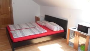 ein kleines Schlafzimmer mit einem Bett mit roter Bettwäsche und Kissen in der Unterkunft Apartman Vilo in Veľký Meder