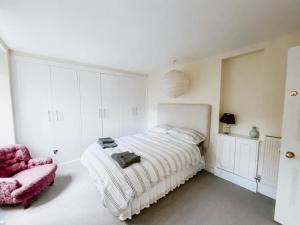 a white bedroom with a bed and a pink chair at SUNNYSIDE APARTMENT - Spacious 2 Bedroom Ground Floor with Free Parking In Kendal, Cumbria in Kendal