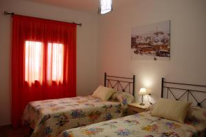 Casa Rural Sierra de las Nieves في Yunquera: غرفة نوم بسريرين ونافذة ذات ستائر حمراء