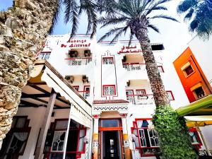 a white building with a palm tree in front of it at Hôtel Auberge du Littoral in Aourir