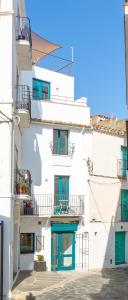 biały budynek z zielonymi drzwiami i balkonami w obiekcie Habitacions Bellaire Cadaqués w mieście Cadaqués