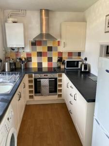 a kitchen with white cabinets and black counter tops at Cosy coastal home - 5 mins walk from the beach in Horton