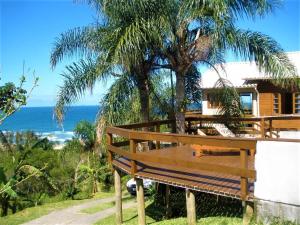 a wooden bench in front of a house with a palm tree at Casa Vista Privilegiada: Piscina e Conforto in Garopaba
