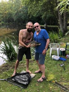 deux hommes debout à côté d'un étang tenant un poisson dans l'établissement Le chalet de Baptiste, à Saint-Michel