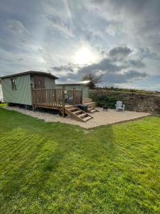 a small green building with a deck and a house at Oakley View Shepherds Hut with hot tub in Whitby