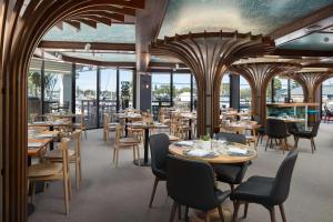 a restaurant with wooden tables and chairs and windows at Sails Port Macquarie by Rydges in Port Macquarie