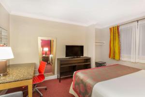 a hotel room with a bed and a desk and a television at Ramada by Wyndham Miami Springs/Miami International Airport in Miami