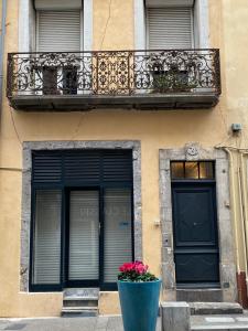 a building with a balcony and a black door and flowers at Le Petit Bijou Sète, quatre appartements au centre ville, trois avec vue canal in Sète