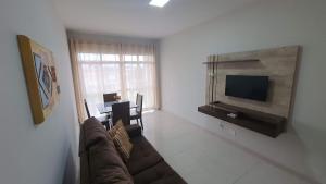 ein Wohnzimmer mit einem Sofa, einem TV und einem Tisch in der Unterkunft Apto 2 Quartos I 2 Banheiros I Guarapari I Por do sol I Wi-Fi in Guarapari
