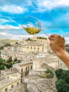 a person holding a glass of wine in front of a city at Bed and Breakfast Terra del Sole Ibla in Ragusa