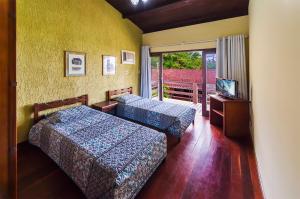 two beds in a room with a television and a balcony at Hotel Pousada do Sol in Ubatuba