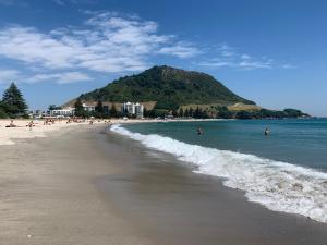 a beach with people in the water and a mountain at Mount Backpackers in Mount Maunganui