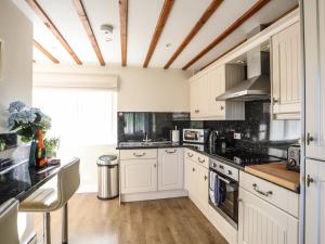 a kitchen with white cabinets and a wooden ceiling at Tyn Towyn - Ty Piws in Trearddur