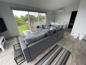 a living room with a gray couch and a large window at Creek to Beach in Apollo Bay