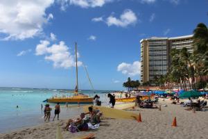 un grupo de personas en una playa con un barco amarillo en Aloha Suites Waikiki en Honolulu