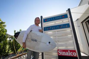 un hombre sosteniendo una tabla de surf delante de un cartel en Guesthouse Petit Pré en Saint-Léonard