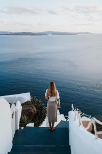 uma mulher de pé numa escada a olhar para a água em Santorini Secret Suites & Spa, Small Luxury Hotels of the World em Oia