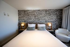 a bedroom with a large white bed and a chair at Hôtel Le Catalogne in Saint-Aygulf