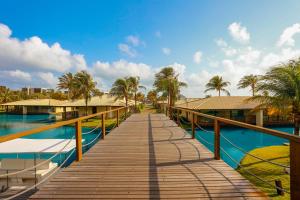 a wooden walkway leading to a pool with palm trees at Dom Pedro Laguna Beach Resort & Golf in Aquiraz