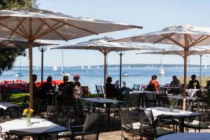 eine Gruppe von Personen, die an Tischen mit Sonnenschirmen sitzen in der Unterkunft Strandhotel SüdSee Diessen am Ammersee in Dießen am Ammersee