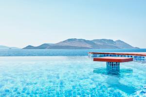 a red bench in the water with mountains in the background at Meis Exclusive Hotel in Kaş