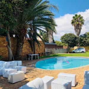 a pool with white chairs and a palm tree at Selina Airport Lodge #Emzini in Kempton Park