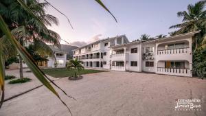 an exterior view of a large white building with palm trees at Jamelah Beach Guest House in Anse aux Pins