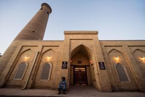 a woman standing in front of a building with a lighthouse at New Star Boutique hotel - madrasah Muhammad Mahram 1903 in Khiva