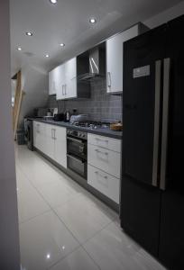 Comfortable stay in Shirley, Solihull - Room 1 في برمنغهام: مطبخ فيه دواليب بيضاء وثلاجة سوداء