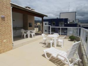 un patio con sillas blancas y mesas en un balcón en Apartamento completo p temporada Ubatuba, excelente localização com conforto e economia, en Ubatuba