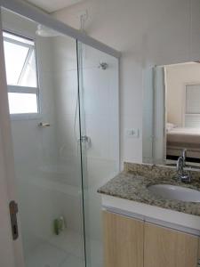 Un baño con ducha de cristal y lavabo. en Apartamento completo p temporada Ubatuba, excelente localização com conforto e economia, en Ubatuba
