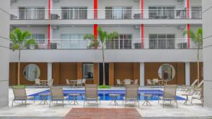 una piscina con sillas y mesas frente a un edificio en Apartamento Praia Grande, en Ubatuba