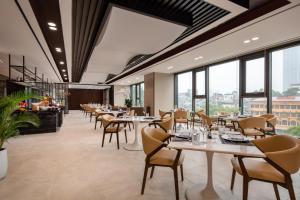 un restaurante con mesas, sillas y ventanas grandes en The Five Residences Hanoi, en Hanói