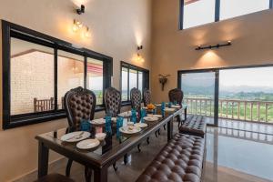 a dining room with a table and chairs and windows at StayVista's Dazzle - Unwind in a Mountain-City View Villa with A Pool and Indoor Activities in Karjat