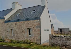 a stone house with a black roof and a wall at La Lanterne du Bout du Monde in Ouessant