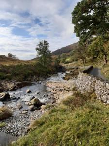 a river with rocks and a stone wall next to a field at Penystryd in Trawsfynydd