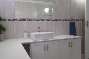 ein weißes Badezimmer mit einem Waschbecken und einem Spiegel in der Unterkunft 18 Steps - Seaside Cottage with breathtaking views in Kapstadt