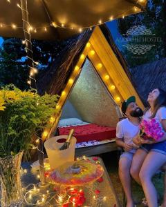 a man and woman sitting in a tent with lights at Smartcamp Ilhabela ᵇʸ ᴬᴸᴱᴮᴬᴴᴸᴵ in Ilhabela