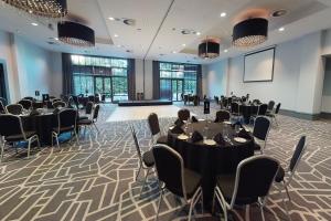 um salão de banquetes com mesas e cadeiras e um ecrã de projecção em Village Hotel London Watford em Elstree