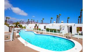 a swimming pool in front of a building with palm trees at Puerto Chico R in Playa Blanca