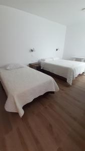 two beds in a white room with wooden floors at Betania in Paracas