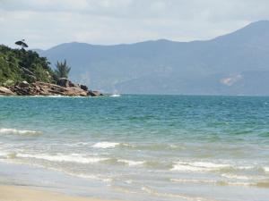 a beach with the ocean and mountains in the background at Casa com piscina para família in Florianópolis