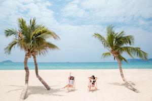 Horizon Resort & Spa Yalong Bay-Yalong Bay Central في سانيا: شخصان يجلسان على الكراسي على الشاطئ بين شجرتي نخيل +183 صورة