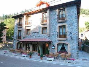 - un grand bâtiment en pierre avec des tables en face dans l'établissement Hotel Cosgaya, à Cosgaya