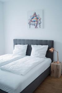 een bed met witte lakens en een schilderij aan de muur bij Prime Park Family Apartment Aschaffenburg in Aschaffenburg