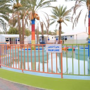 uma piscina com palmeiras e uma placa numa cerca em بيرحاء إبراء للسياحة em Ibrā