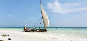 a sail boat on a beach with people in the water at ARYA Boutique Resort in Kiwengwa